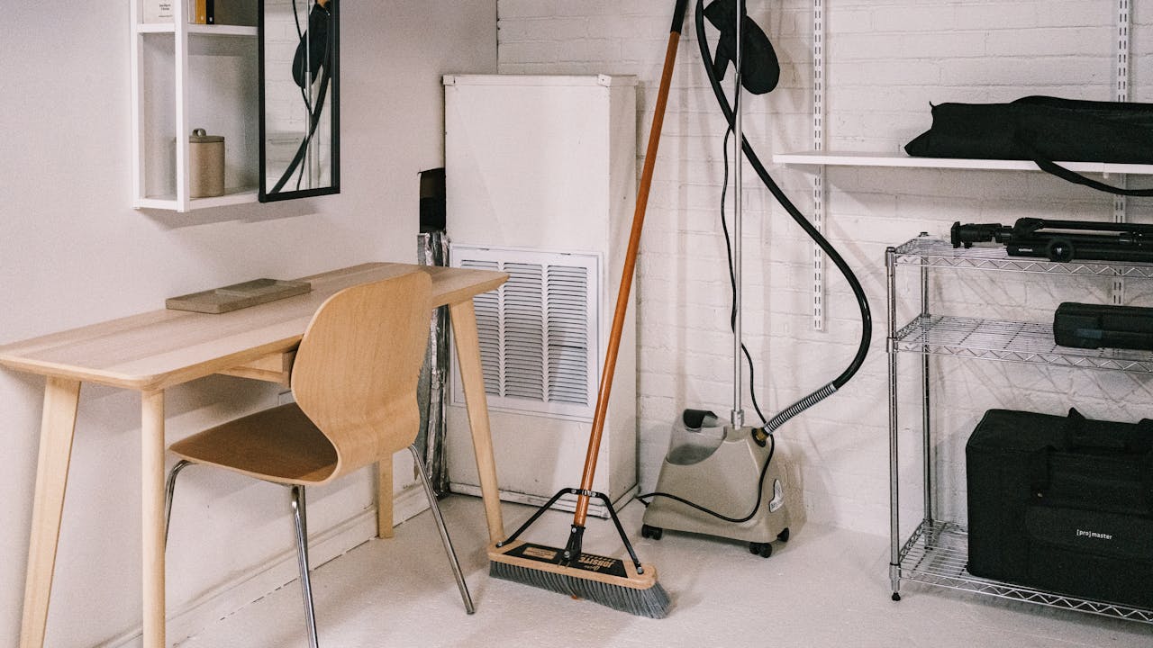 about-01 A tidy home office space featuring a wooden desk, chair, broom, and cleaning equipment.